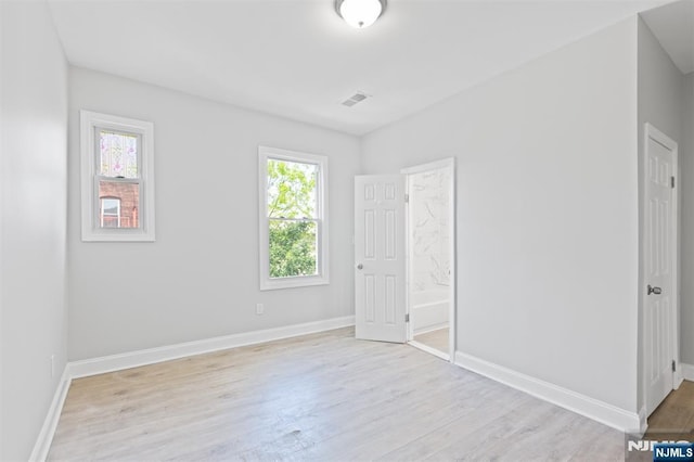 unfurnished bedroom with light wood finished floors, baseboards, and ensuite bath