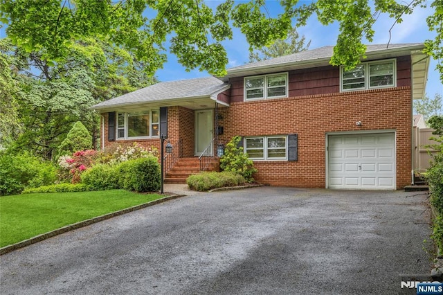 tri-level home with an attached garage, driveway, brick siding, and a front lawn