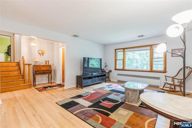 living room featuring radiator heating unit, wood finished floors, stairway, and baseboards