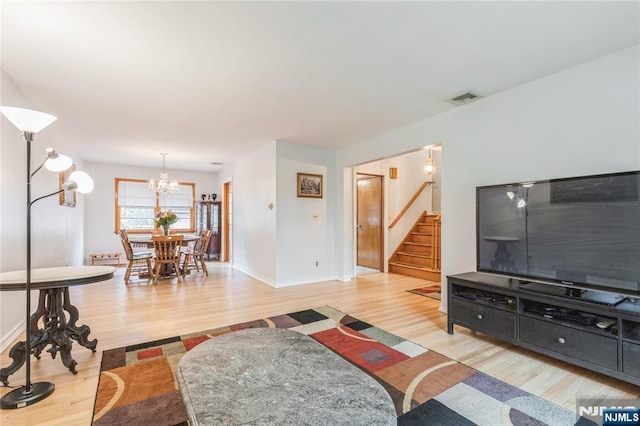 living room featuring light wood finished floors, stairs, baseboards, and a chandelier