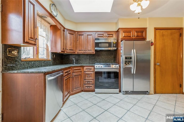 kitchen with appliances with stainless steel finishes, decorative backsplash, a skylight, and light tile patterned floors
