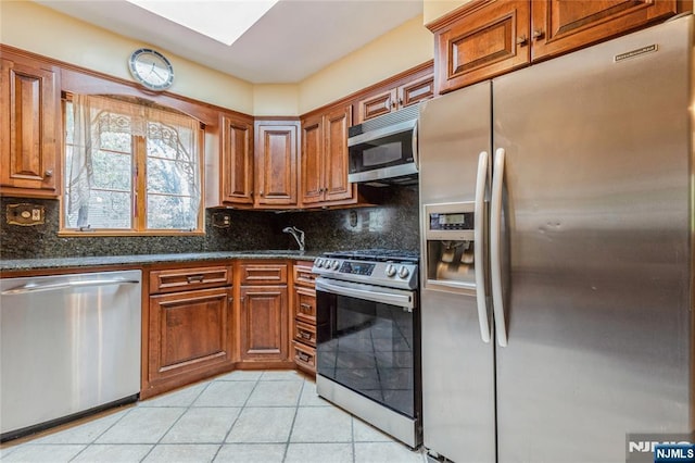 kitchen featuring appliances with stainless steel finishes, light tile patterned floors, backsplash, and a sink
