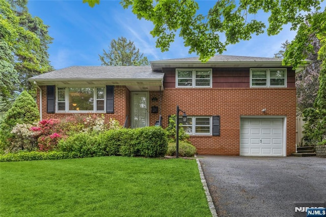 tri-level home with a garage, driveway, a front yard, and brick siding