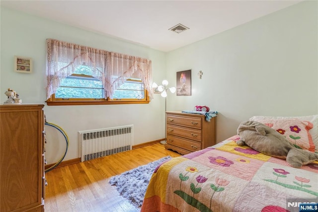 bedroom with radiator heating unit, light wood-type flooring, and baseboards