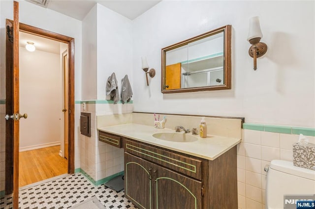 bathroom featuring tile walls, vanity, wainscoting, and toilet