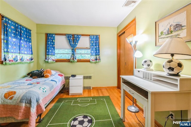 bedroom with radiator, wood finished floors, and baseboards
