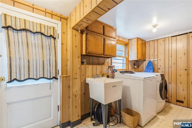 clothes washing area with cabinet space, washing machine and clothes dryer, light flooring, and wood walls