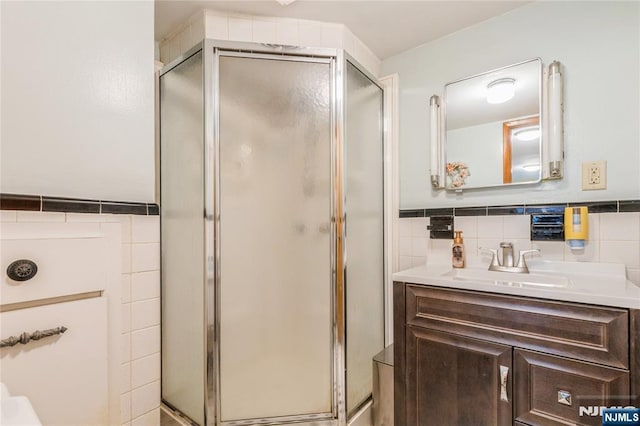 full bath with tile walls, a shower stall, vanity, and wainscoting