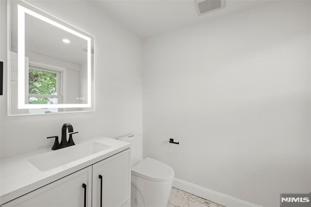bathroom featuring marble look tile flooring, toilet, vanity, and baseboards