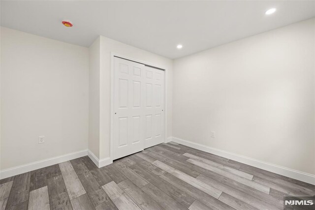 unfurnished bedroom with wood finished floors, baseboards, recessed lighting, and a closet