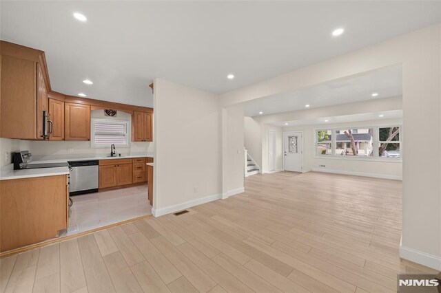 kitchen featuring stainless steel dishwasher, open floor plan, a sink, light wood finished floors, and light countertops