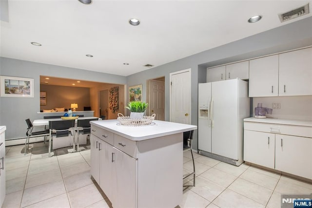 kitchen with white refrigerator with ice dispenser, a kitchen island, light countertops, a kitchen bar, and a baseboard heating unit