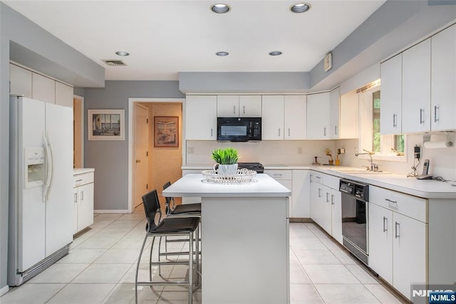 kitchen featuring black appliances, light countertops, a breakfast bar, a kitchen island, and light tile patterned floors