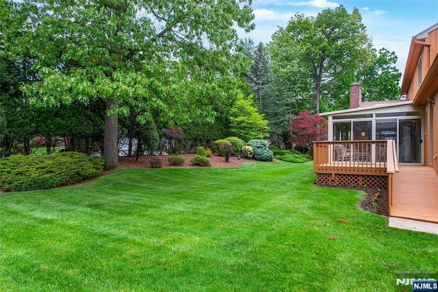 view of green lawn featuring a sunroom and a wooden deck