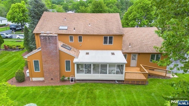 rear view of house featuring a lawn, a sunroom, a shingled roof, and a deck