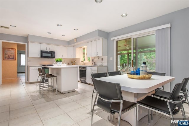kitchen featuring black microwave, a kitchen island, a kitchen breakfast bar, white cabinets, and light countertops