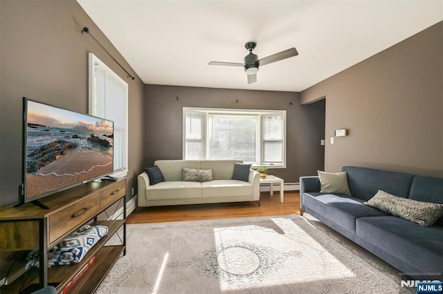 living area featuring wood finished floors, a ceiling fan, baseboards, and a baseboard heating unit