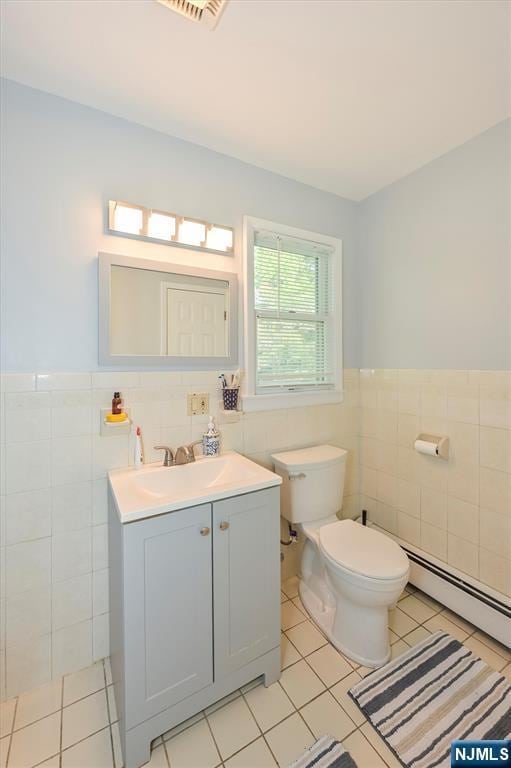 half bath featuring tile walls, tile patterned floors, toilet, wainscoting, and vanity