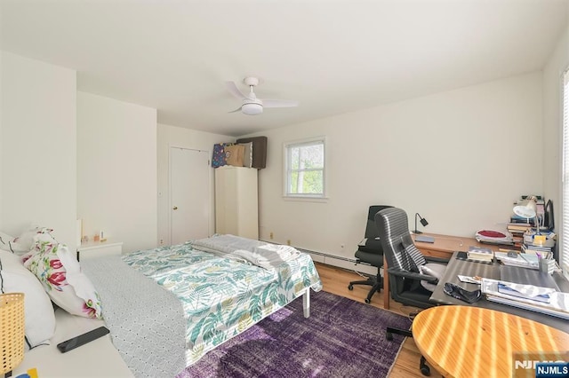 bedroom with wood finished floors, a baseboard heating unit, an office area, and a ceiling fan