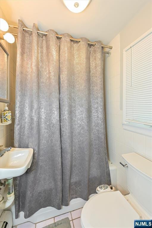 bathroom featuring tile walls, toilet, shower / tub combo, a sink, and tile patterned floors