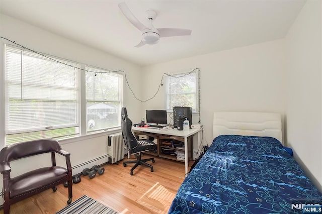 bedroom featuring radiator heating unit, light wood finished floors, a desk, and a ceiling fan