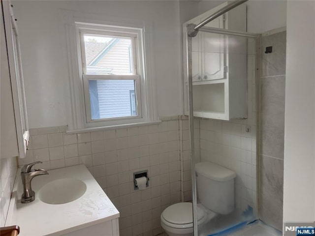 bathroom with tile walls, a stall shower, toilet, and vanity