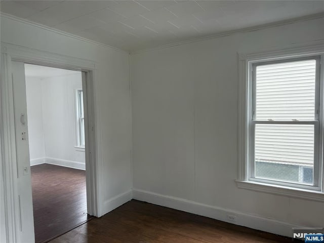 empty room with ornamental molding, dark wood-style flooring, and baseboards