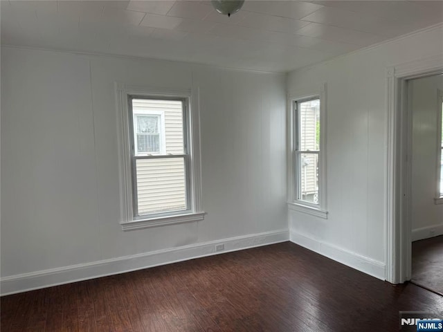 empty room featuring dark wood-type flooring, baseboards, and crown molding