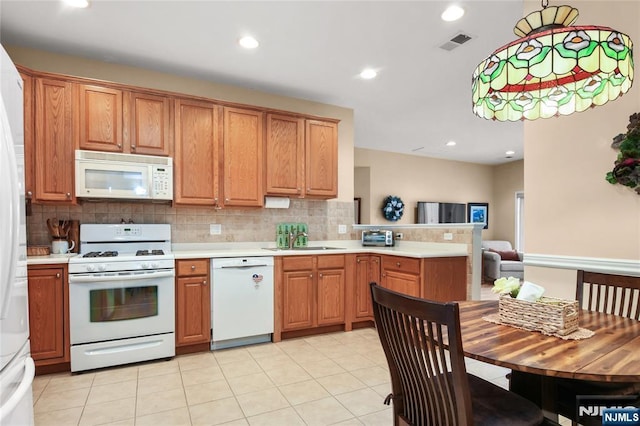 kitchen featuring white appliances, light countertops, decorative backsplash, a peninsula, and a sink
