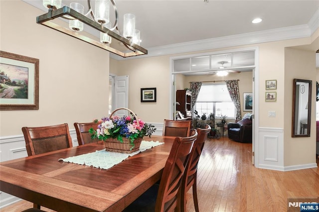 dining area featuring ornamental molding, a wainscoted wall, light wood finished floors, a chandelier, and a decorative wall