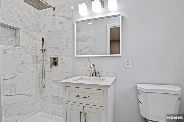 full bathroom featuring tiled shower, vanity, and toilet
