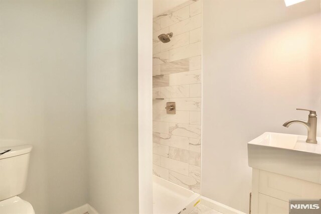 full bathroom with tiled shower, marble finish flooring, toilet, and baseboards
