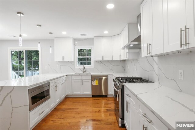 kitchen featuring stainless steel appliances, a sink, white cabinets, wall chimney range hood, and decorative backsplash