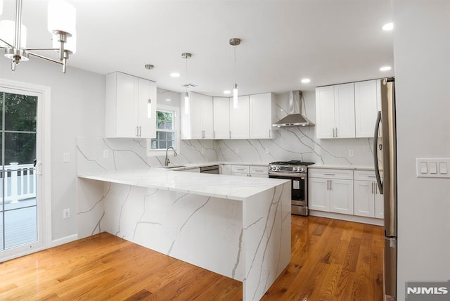 kitchen featuring stainless steel appliances, wall chimney exhaust hood, a peninsula, light wood-type flooring, and a sink