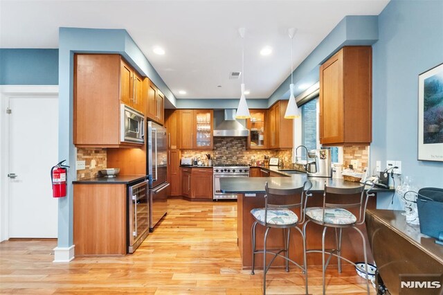 8709 Churchill Rd, North Bergen, NJ 07047 - kitchen featuring high end appliances, wall chimney exhaust hood, a sink, brown cabinetry, and a peninsula