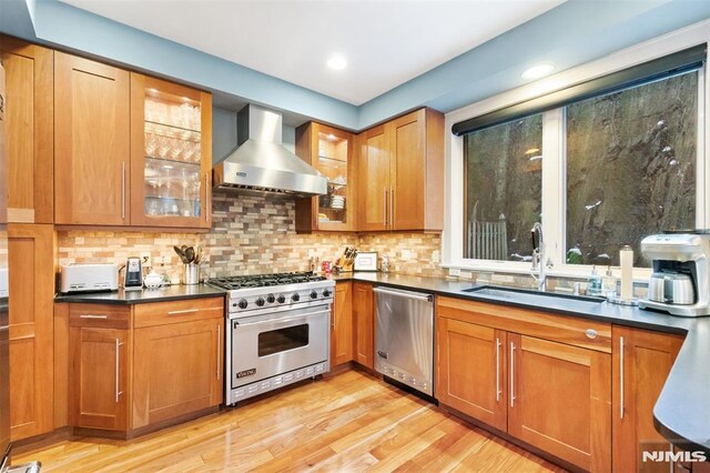 8709 Churchill Rd, North Bergen, NJ 07047 - kitchen featuring stainless steel appliances, a sink, wall chimney exhaust hood, brown cabinets, and light wood-type flooring