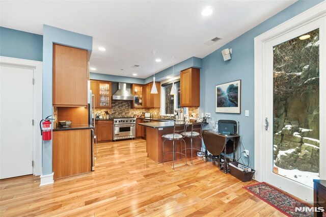 8709 Churchill Rd, North Bergen, NJ 07047 - kitchen featuring stainless steel range, wall chimney exhaust hood, a peninsula, brown cabinets, and recessed lighting