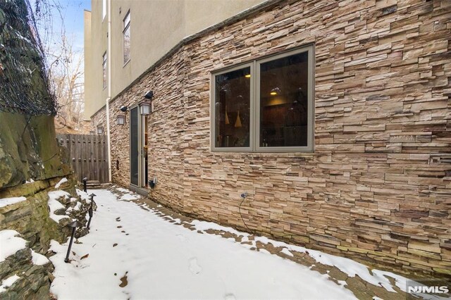 8709 Churchill Rd, North Bergen, NJ 07047 - view of snowy exterior featuring stone siding, fence, and stucco siding