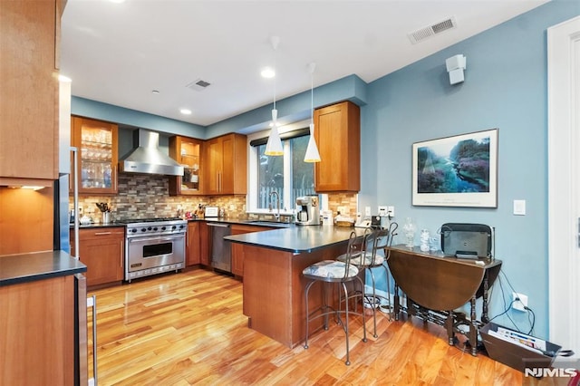 8709 Churchill Rd, North Bergen, NJ 07047 - kitchen with stainless steel appliances, wall chimney range hood, a sink, a peninsula, and brown cabinets