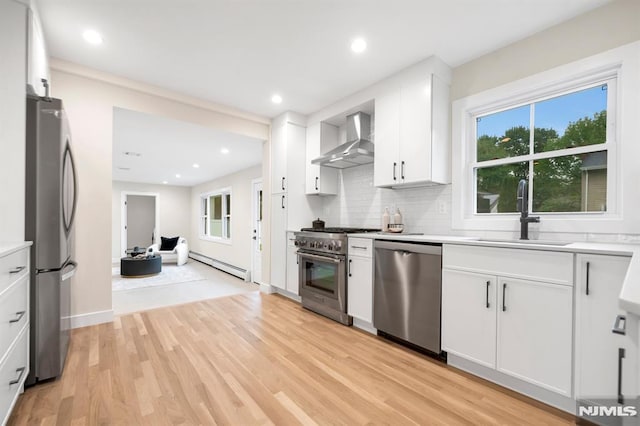 246 Oakwood Dr, Paramus, NJ 07652 - kitchen with appliances with stainless steel finishes, wall chimney range hood, a sink, a baseboard heating unit, and light wood-style floors