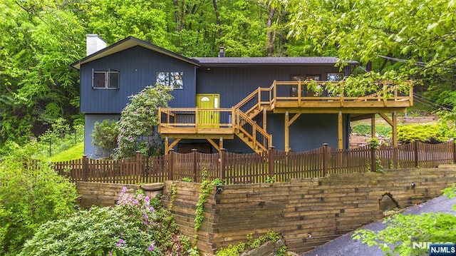 view of front of property featuring a deck, a chimney, stairway, a fenced backyard, and a forest view