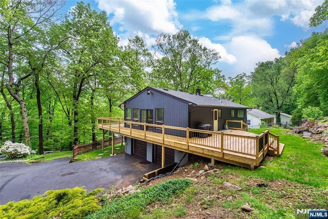 rear view of house with a wooden deck, an attached garage, driveway, and fence
