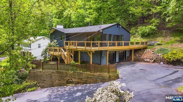 view of front facade featuring a wooden deck, an attached garage, asphalt driveway, fence, and stairway