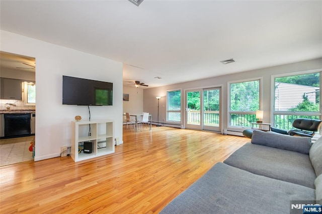 living area with a ceiling fan, healthy amount of natural light, light wood finished floors, and baseboard heating