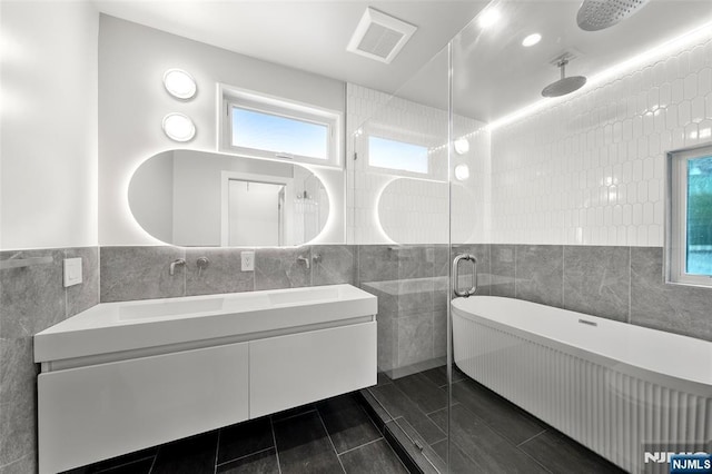 full bathroom with tile walls, double vanity, a tile shower, a freestanding bath, and tile patterned flooring