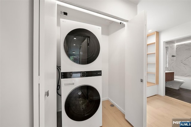washroom with stacked washer / drying machine and wood finished floors