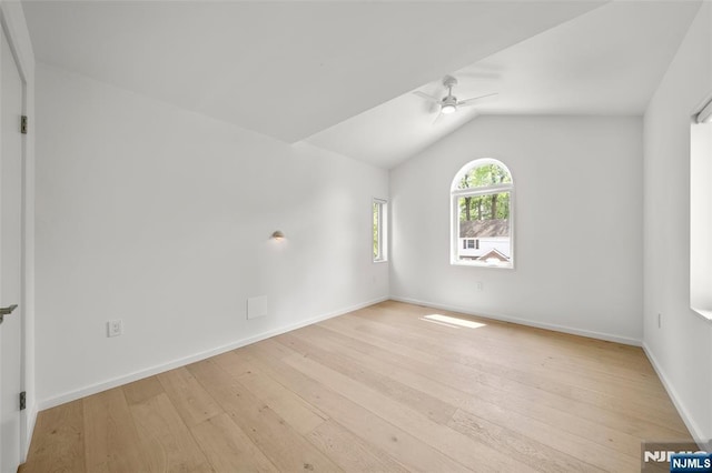 spare room featuring ceiling fan, light wood-type flooring, lofted ceiling, and baseboards