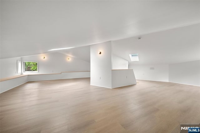 additional living space with lofted ceiling, light wood-style flooring, and a skylight