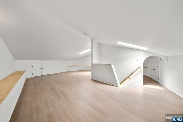 additional living space with arched walkways, vaulted ceiling, and wood finished floors
