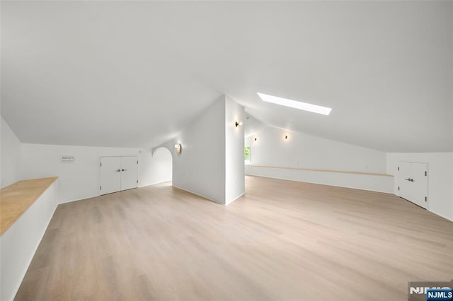 bonus room with lofted ceiling, a skylight, and light wood-style floors